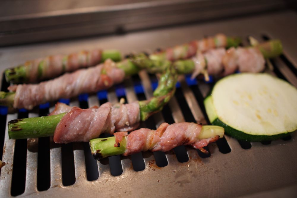 Bacon-wrapped asparagus sizzling on the charcoal tabletop grill with zucchini slices