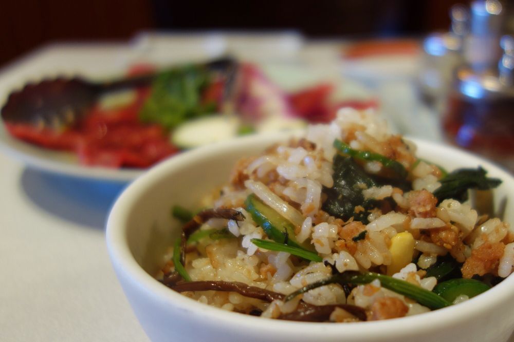 Bibimbap rice bowl with seasoned vegetables and ground chicken, beef plates in background