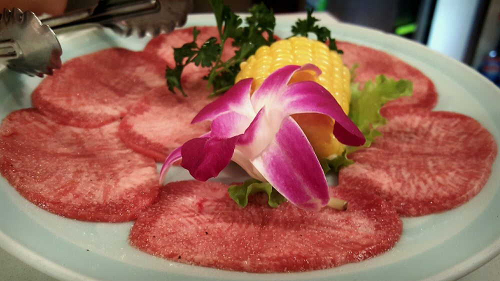 Thinly sliced beef arranged in a circle on a plate with orchid garnish and corn