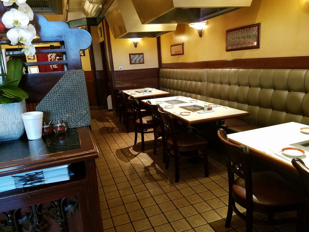 Anjin interior with olive-green leather booths, tabletop charcoal grills, and overhead vent hoods